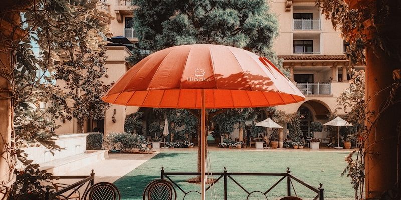 Outdoor cafe seating with large red umbrella and building.