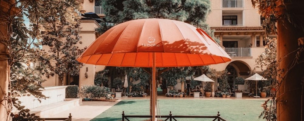 Outdoor cafe seating with large red umbrella and building.
